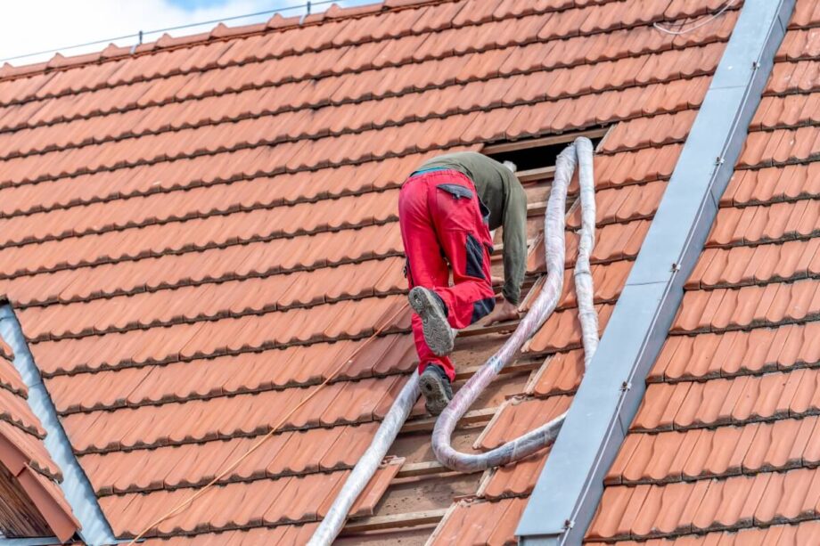 Robotnik na dachu wykonuje ocieplanie celulozą.